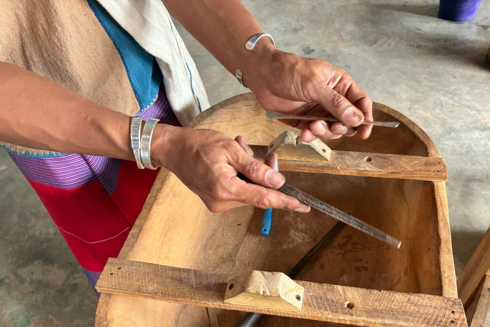 The silversmith filing a piece by hand at the workshop, wearing Karen woven cloth and his own silver bracelets