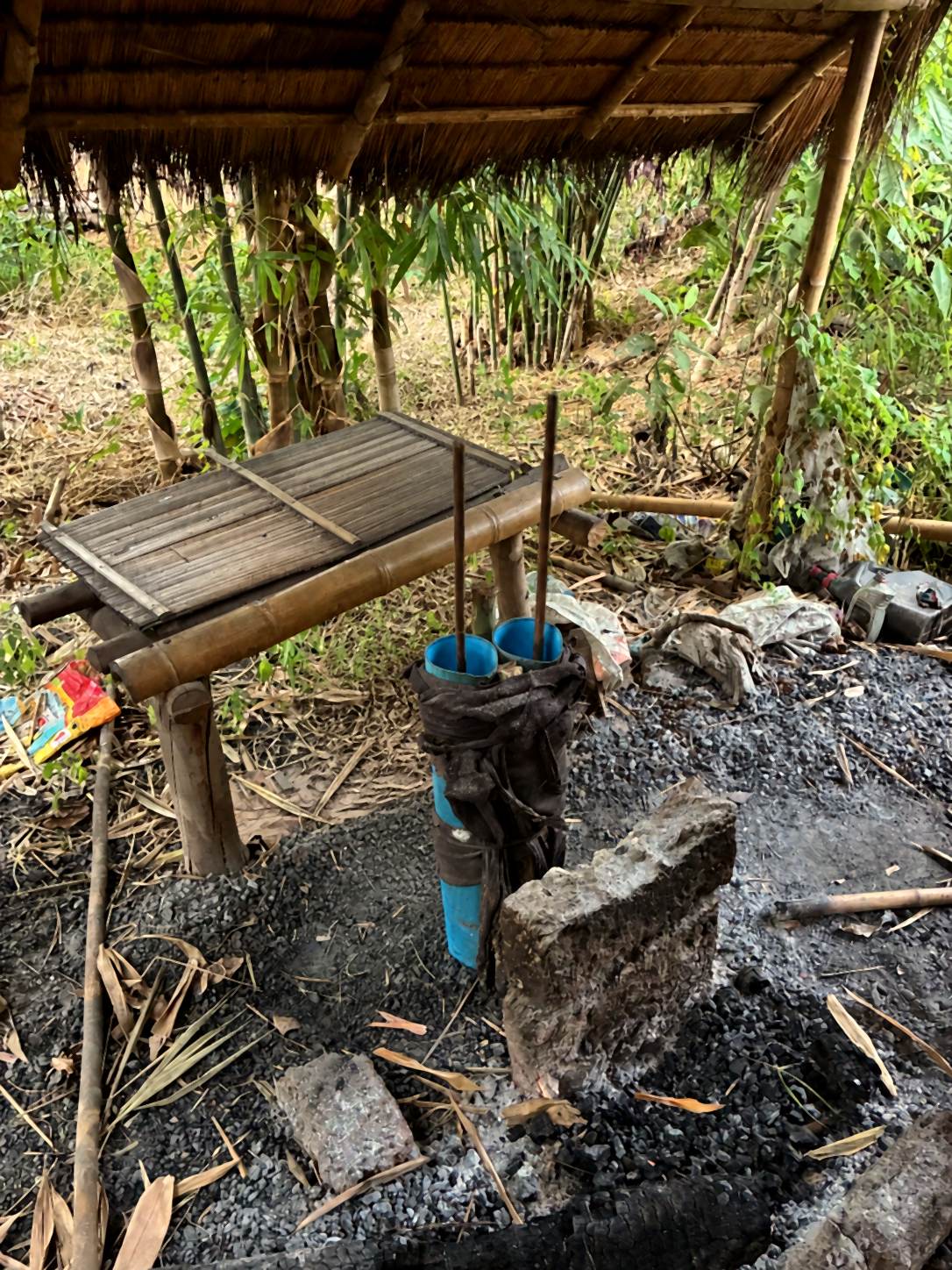 A hand bellows made from blue PVC pipe beside a charcoal bed at a village forge