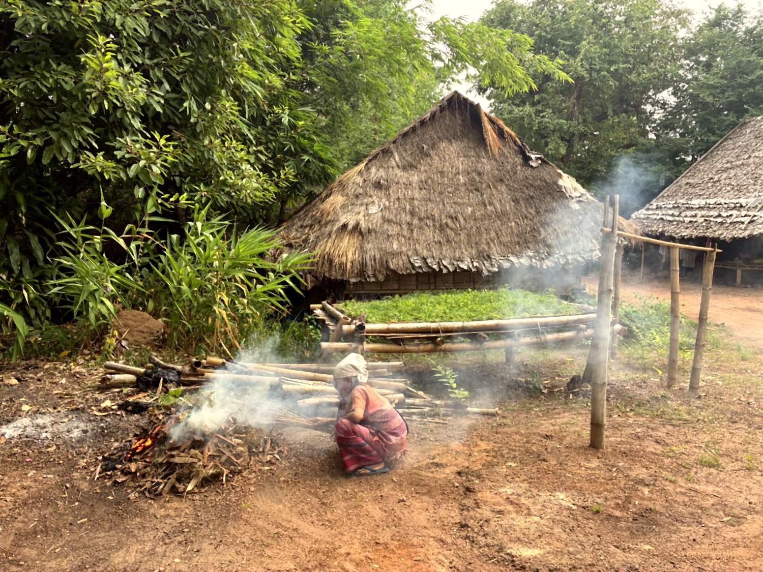 A woman lighting a cooking fire outside a thatched house